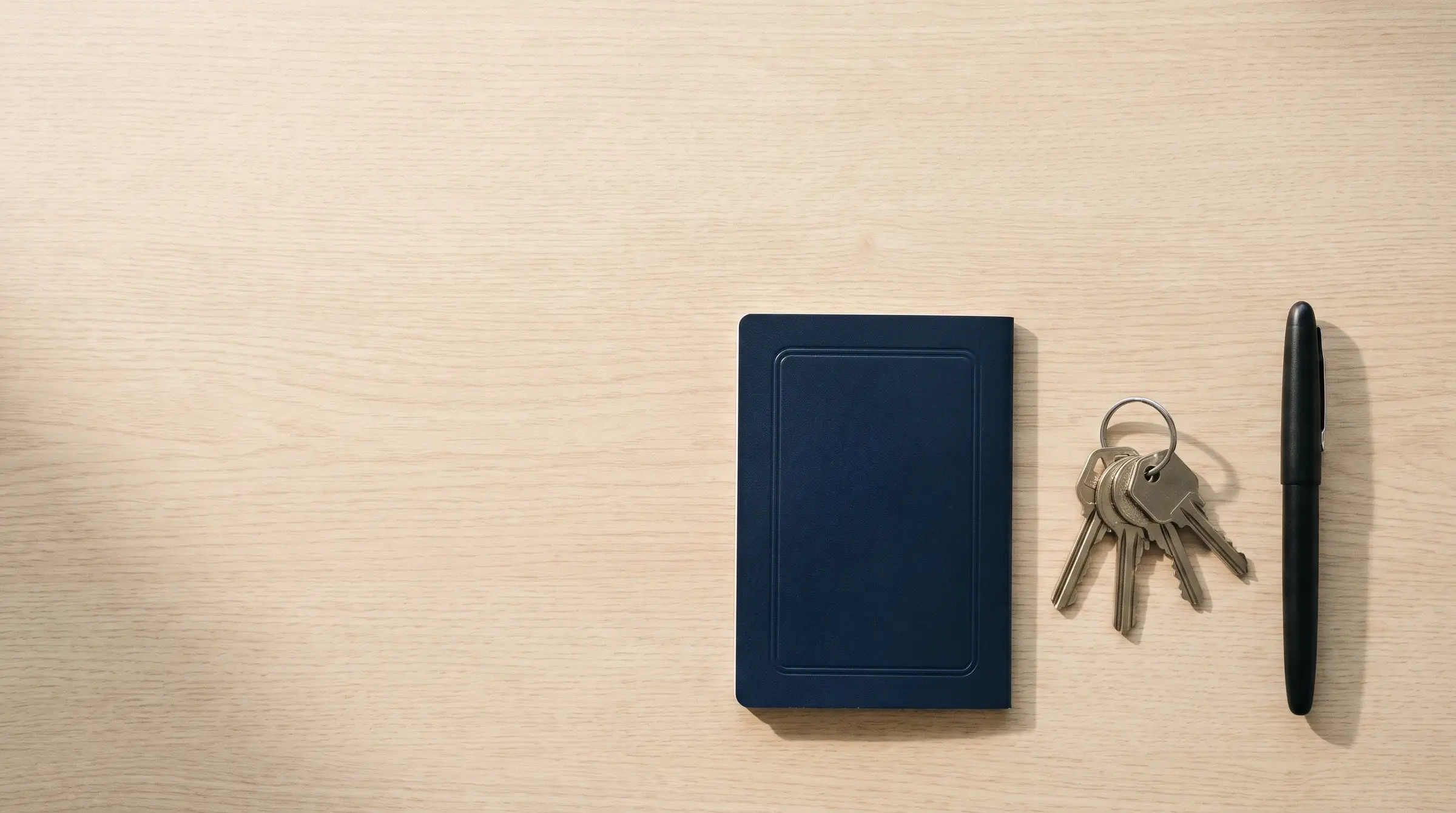 Un pasaporte, un juego de llaves y una pluma sobre un escritorio de madera clara